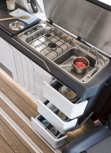 Une cuisine discrète dont les équipements supérieurs sont masqués par un lourd capot. Son ouverture masque totalement la fenêtre.