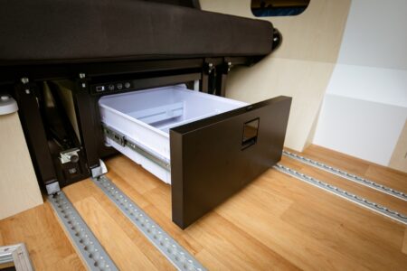 Unik Van - Le réfrigérateur suit la banquette. L'accès devient totalement impossible avec la transformation de celle-ci en couchage.