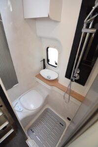 L’espace toilette réunit un WC banc, une petite vasque d’angle et une douche. L’aération est assurée par une baie.