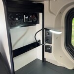 Derrière un rideau à lamelles, les commandes du chauffage Webasto et du chauffe-eau Whale fonctionnant au gaz et sur le réseau 220 V.