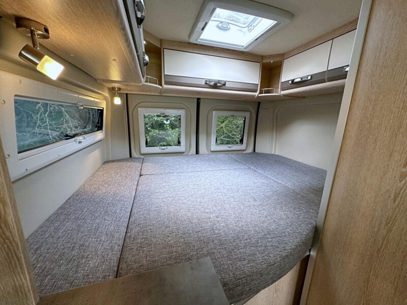 Le Summit 600 B Plus est équipé d'un lit transversal de belles dimensions (160/147 x 196 cm). On apprécie les nombreux rangements en partie haute (cinq placards de pavillon et deux niches.) chambre lit transversal fourgon Pössl Summit 600 B Plus