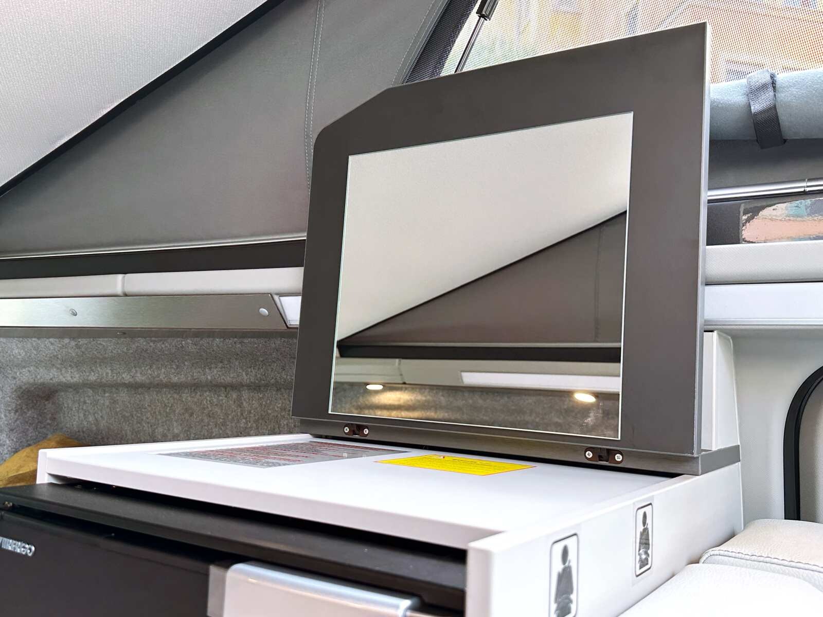 Une coiffeuse avec miroir escamotable se cache au dessus du frigo.