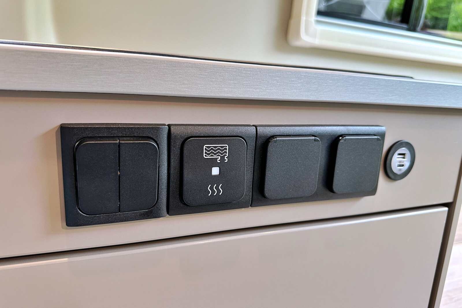 Entre les interrupteurs des spots Leds, et les prises 220V / USB, le bouton lumineux permet d'activer le chauffage des réservoirs d'eaux usées (en option).
