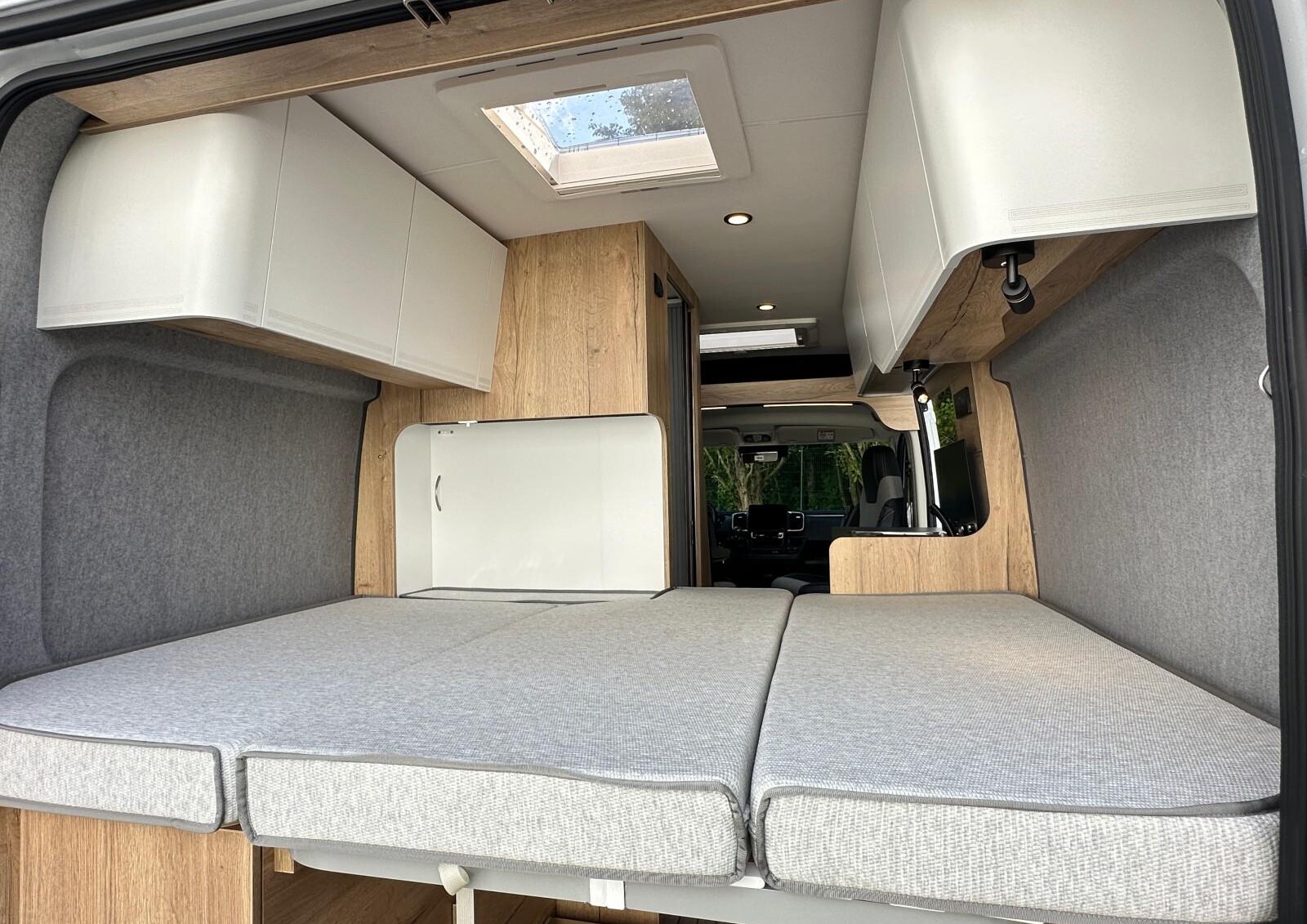 Clever Vans Tour 540 - Pour étendre le lit au maximum de sa largeur, il faut au préalable rétracter la paroi flexible de la salle d'eau, tirer l'extension de sommier et placer le complément de matelas.