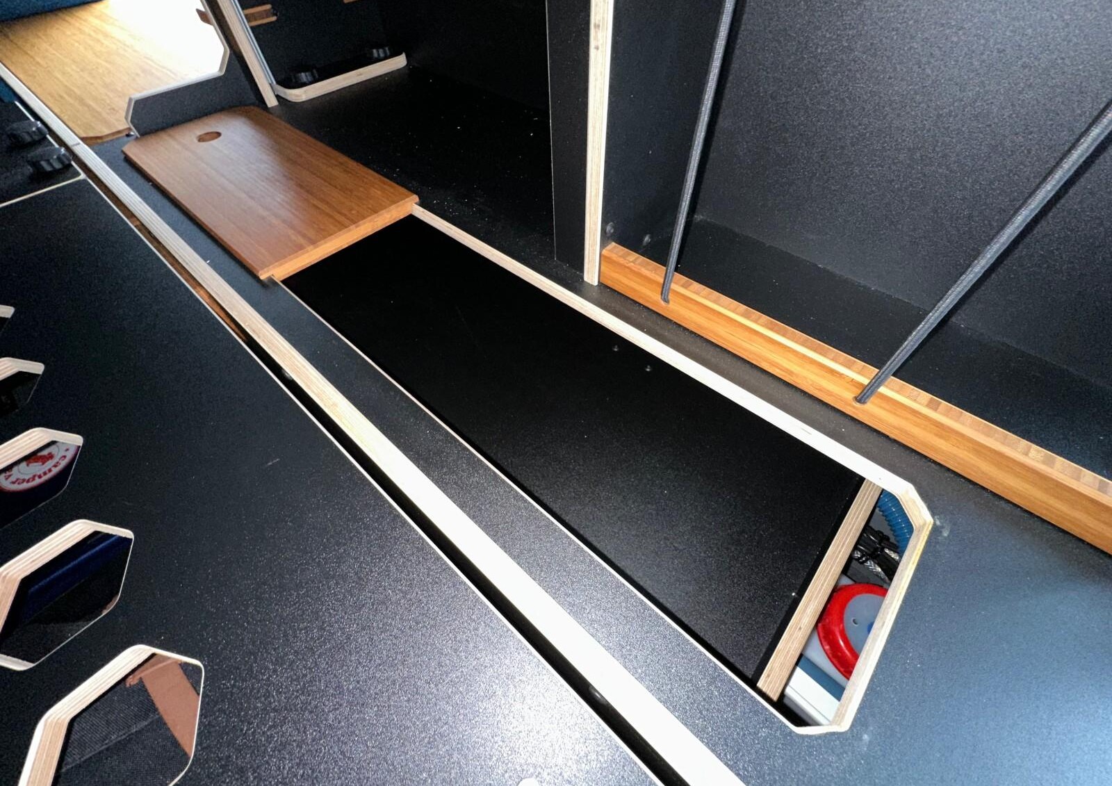 Trappe de rangement nichée au pied du grand meuble latéral, sous le matelas.