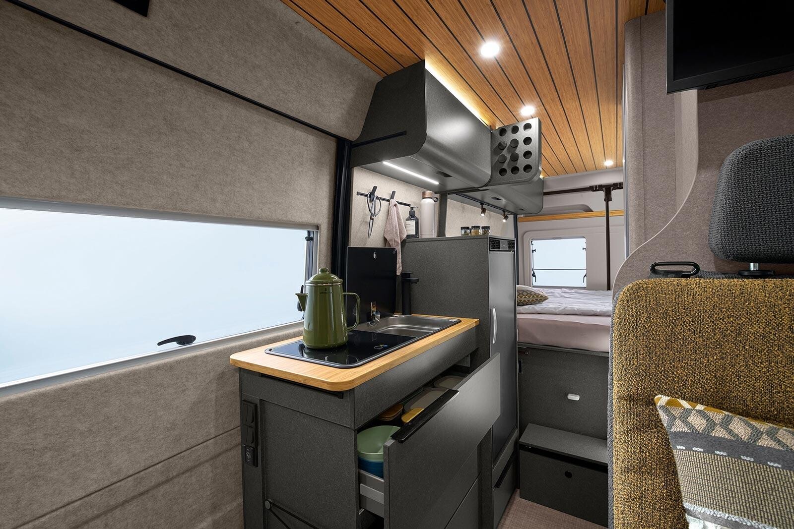 Hymer Redwood. Les tiroirs de la cuisine sont dotés d'une fermeture soft-close. La marche d'accès au lit est articulée. Elle peut s'effacer pour laisser l'arrêt de charge coulisser vers la droite et libérer l'accès ) la soute. Cuisine fourgon Hymer Redwood