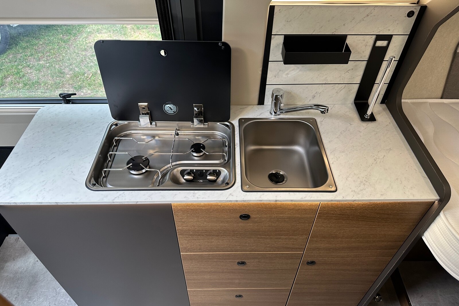 BENIMAR Benivan 160 Plus - Auparavant intégré en hauteur, dans un meuble attenant au lit, le frigo est ici déplacé sous le bloc cuisine, dans l'entrée, afin d'être accessible de l'intérieur comme de l'extérieur.